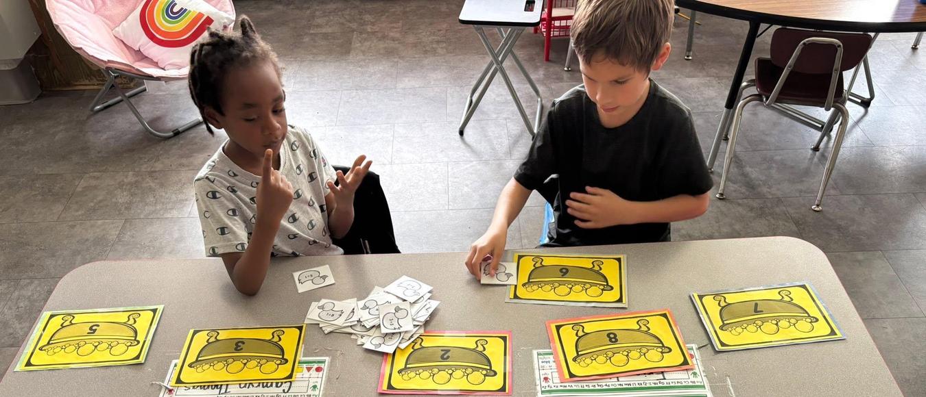 Two young students practice counting with yellow numbered duck mats and small paper cards.