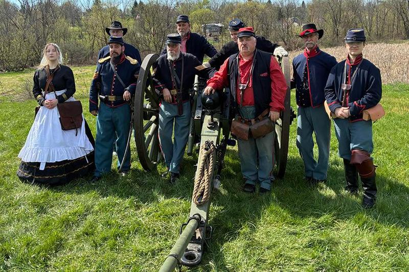 9 members of the 4th U.S. Light Artillery Battery F stands in a field with a canon
