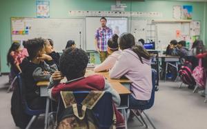 Students attentively watch a teacher presenting in a classroom setting.