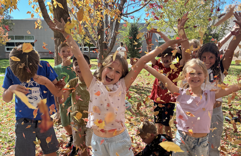 Third graders joyfully throw autumn leaves into the air during recess.
