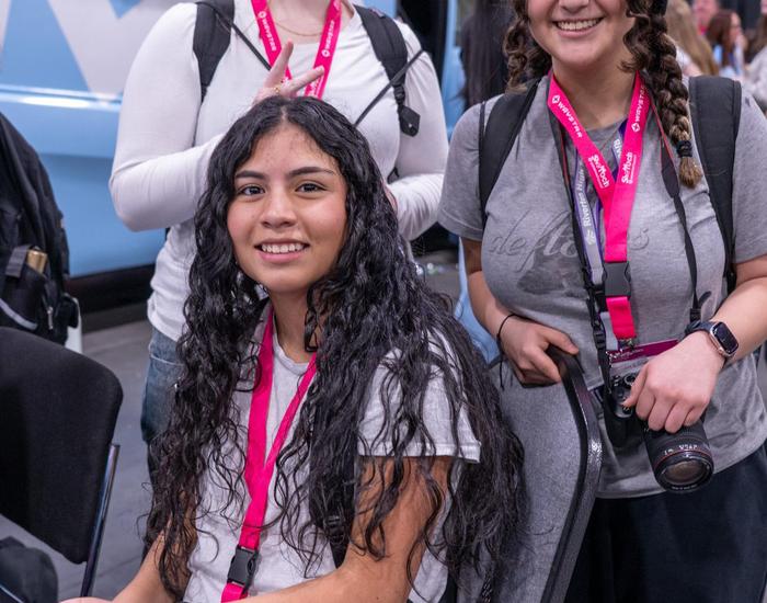 students sitting at SheTech booth smiling at camera