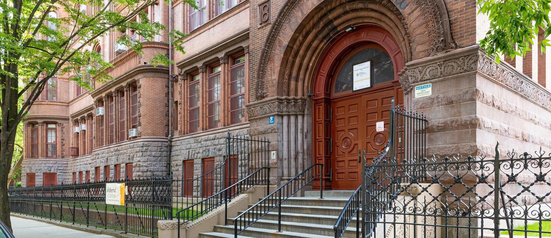 Historic school entrance with ornate brickwork and steps leading to a wooden door.