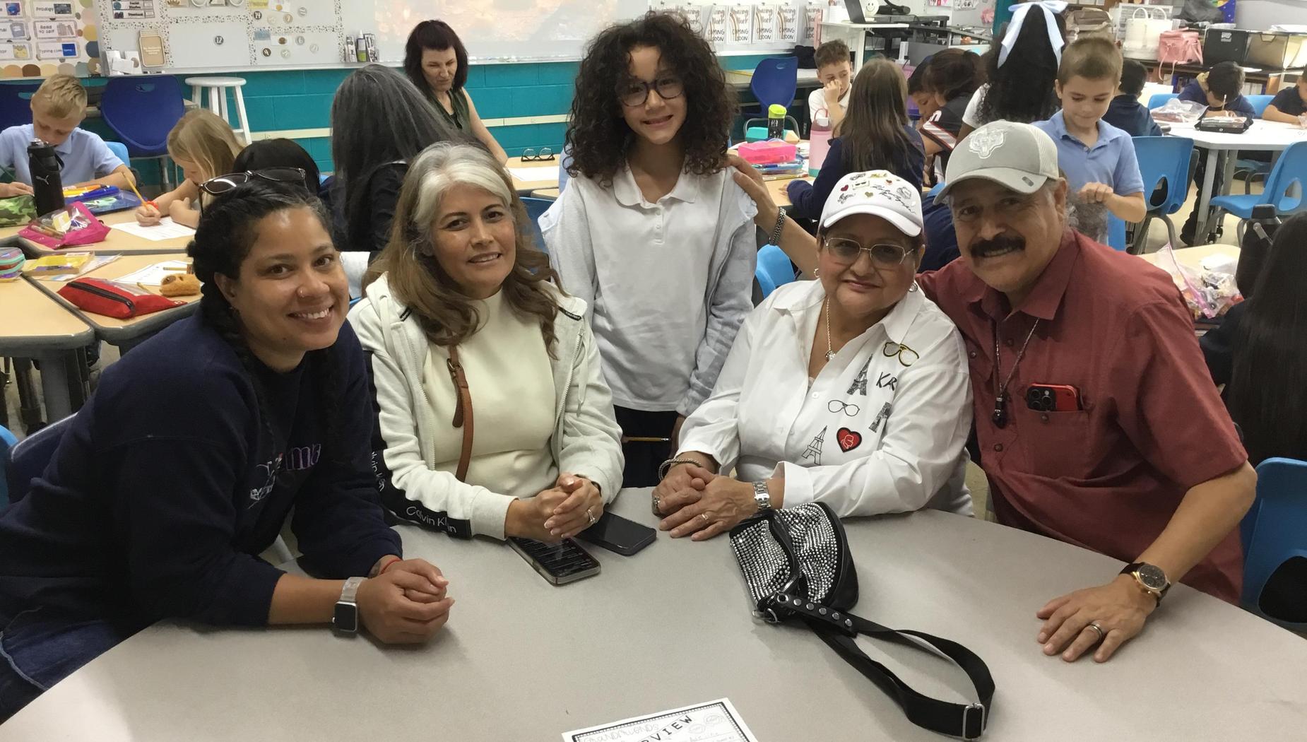 A group of five people smiling together at a classroom table.