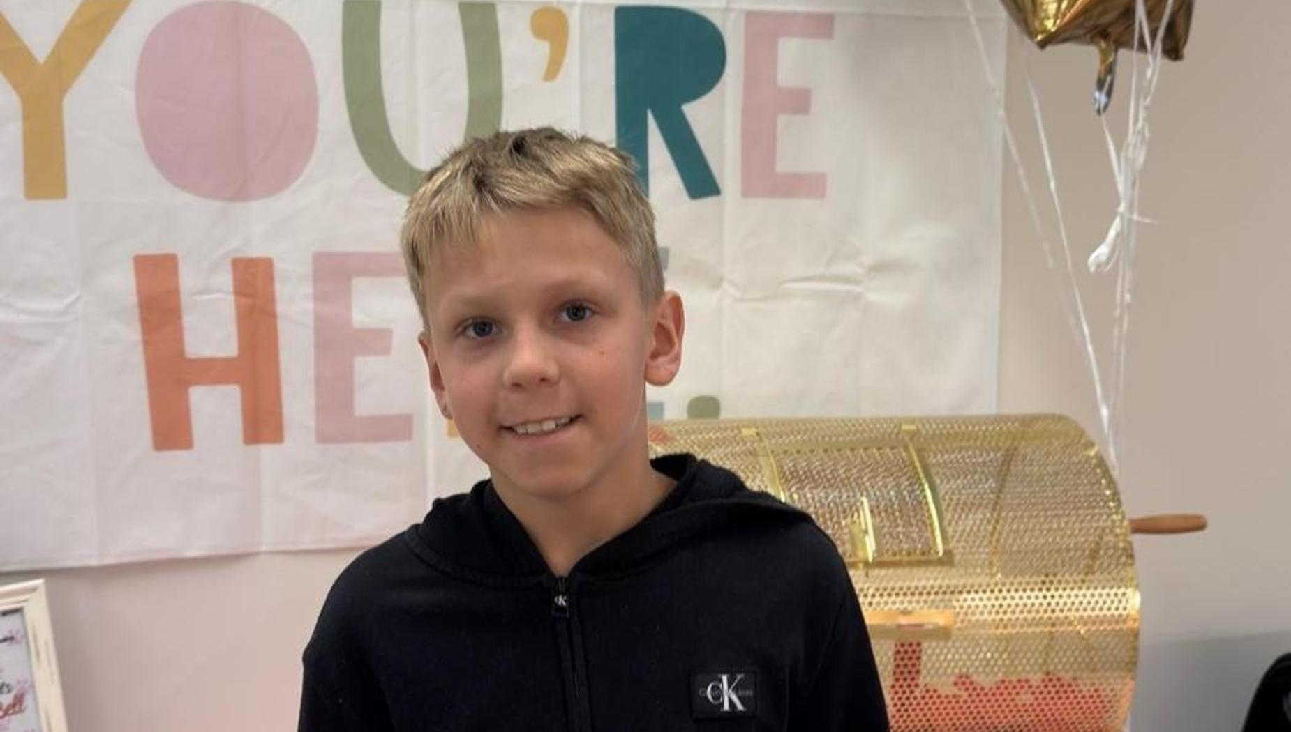 A boy smiles in front of a colorful banner and a golden raffle drum.