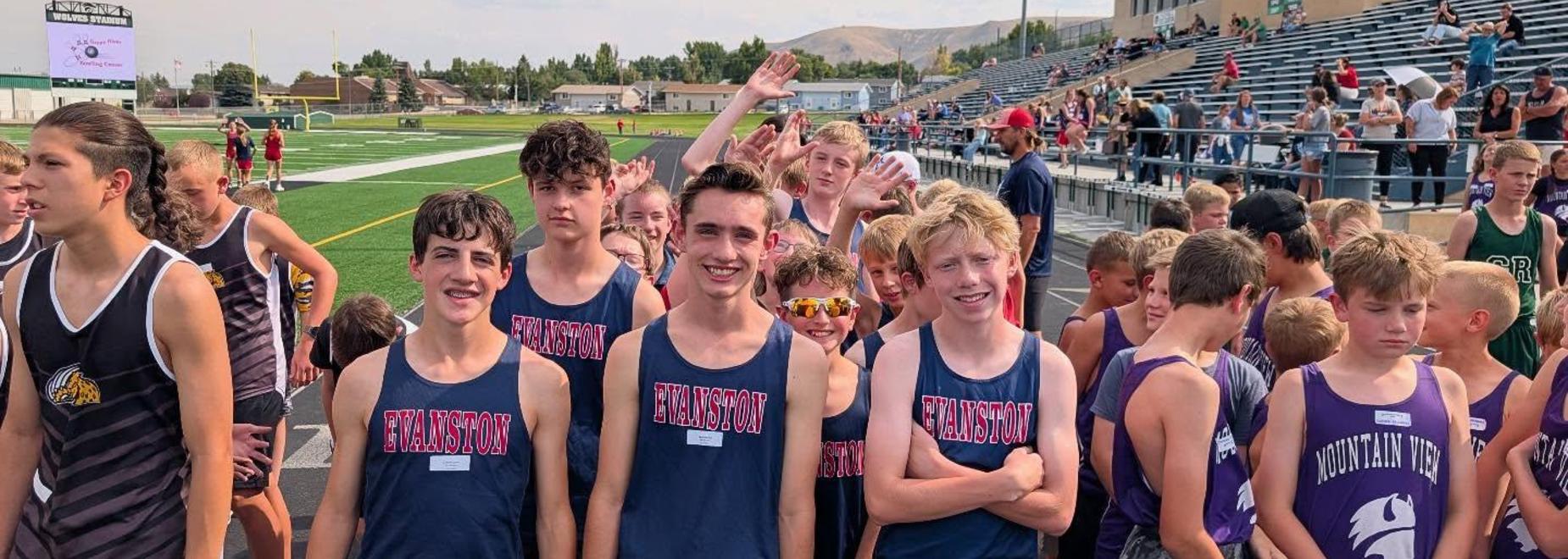 Group of male athletes in tank tops smiling and posing after a race on a sports field.