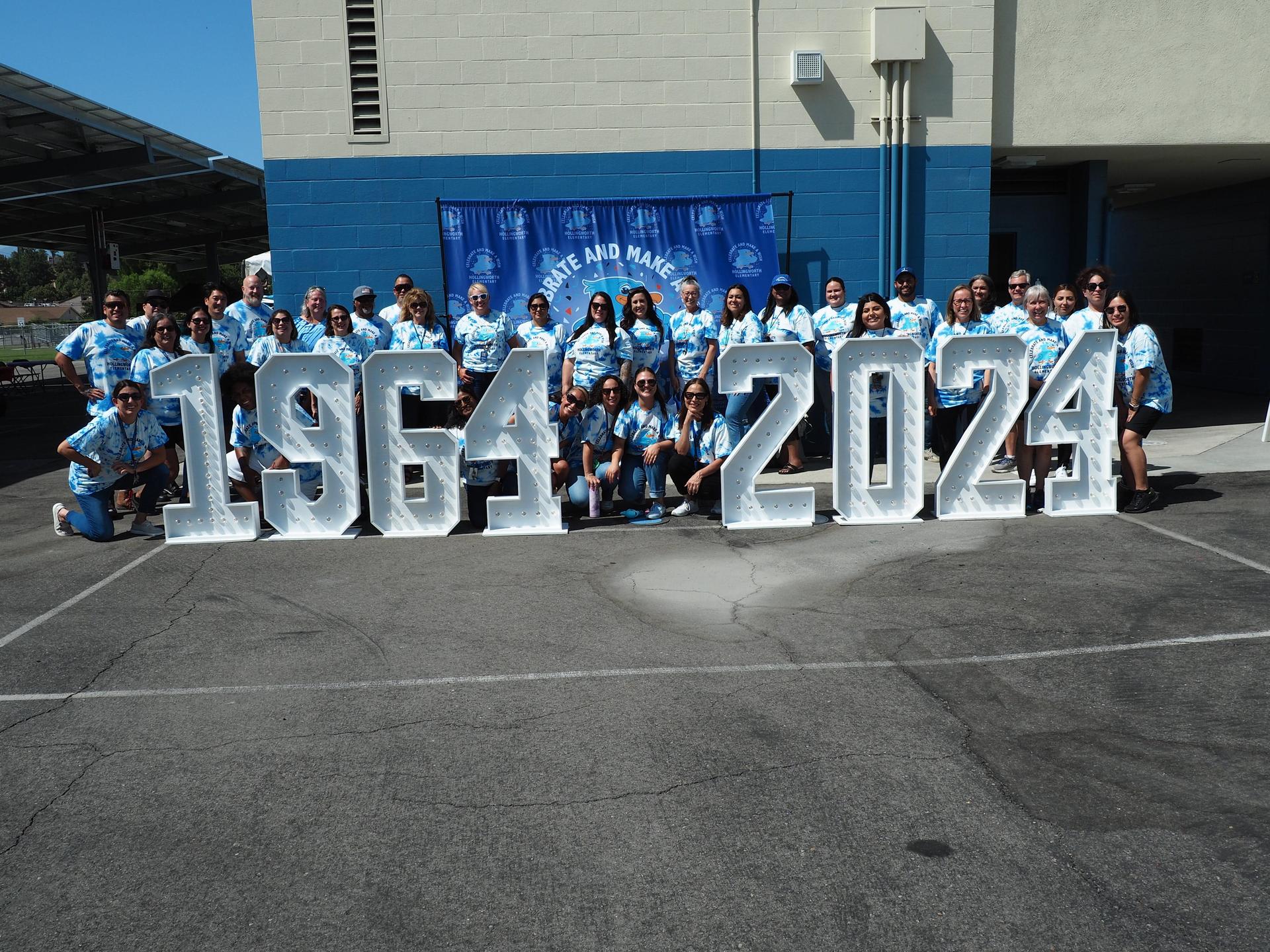 Picture of Hollingworth staff in front of 1964-2024 signs for our 60th anniversary event