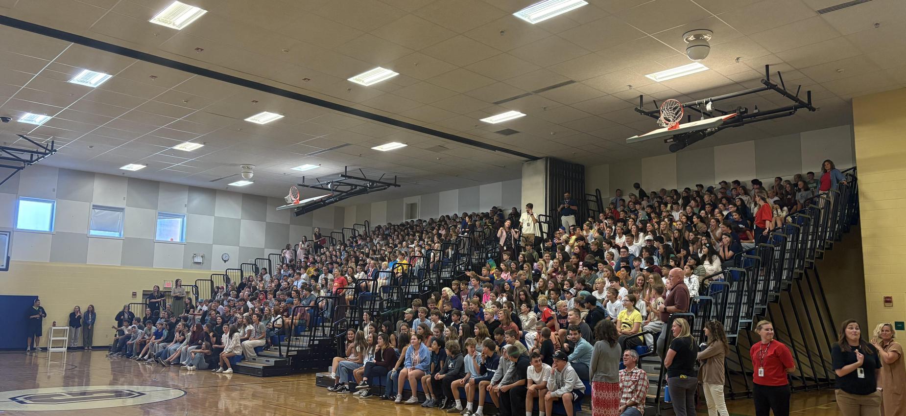 A large crowd of students seated in a gymnasium during an assembly.