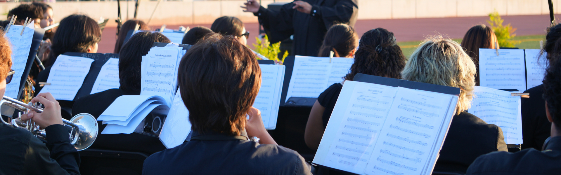View of musicians from behind as they play, with sheets of music visible.