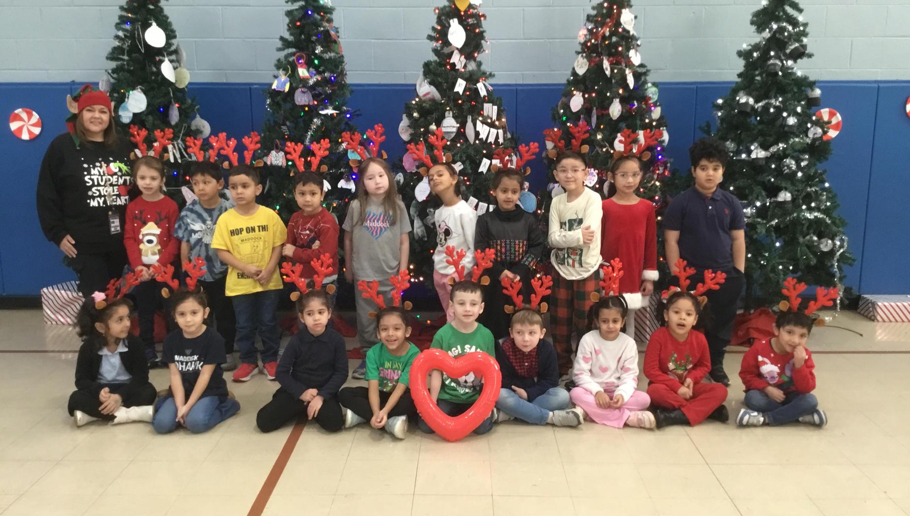 A group of children and an adult posing in front of decorated Christmas trees.