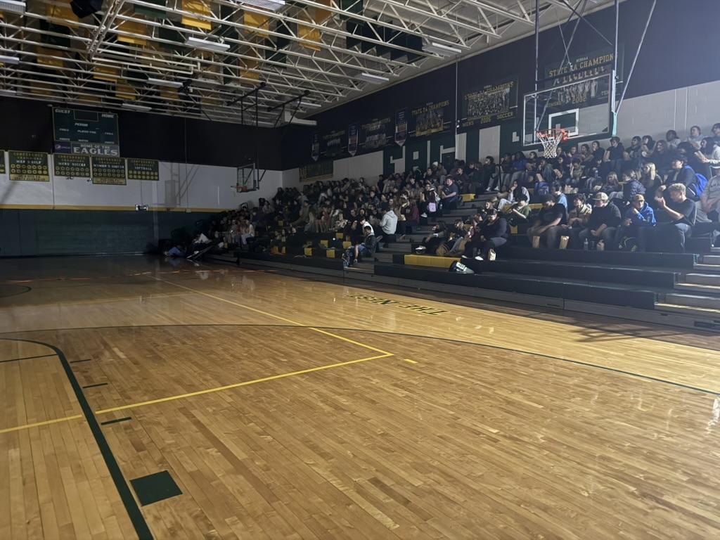 A crowded gymnasium with spectators sitting in bleachers, watching an event.