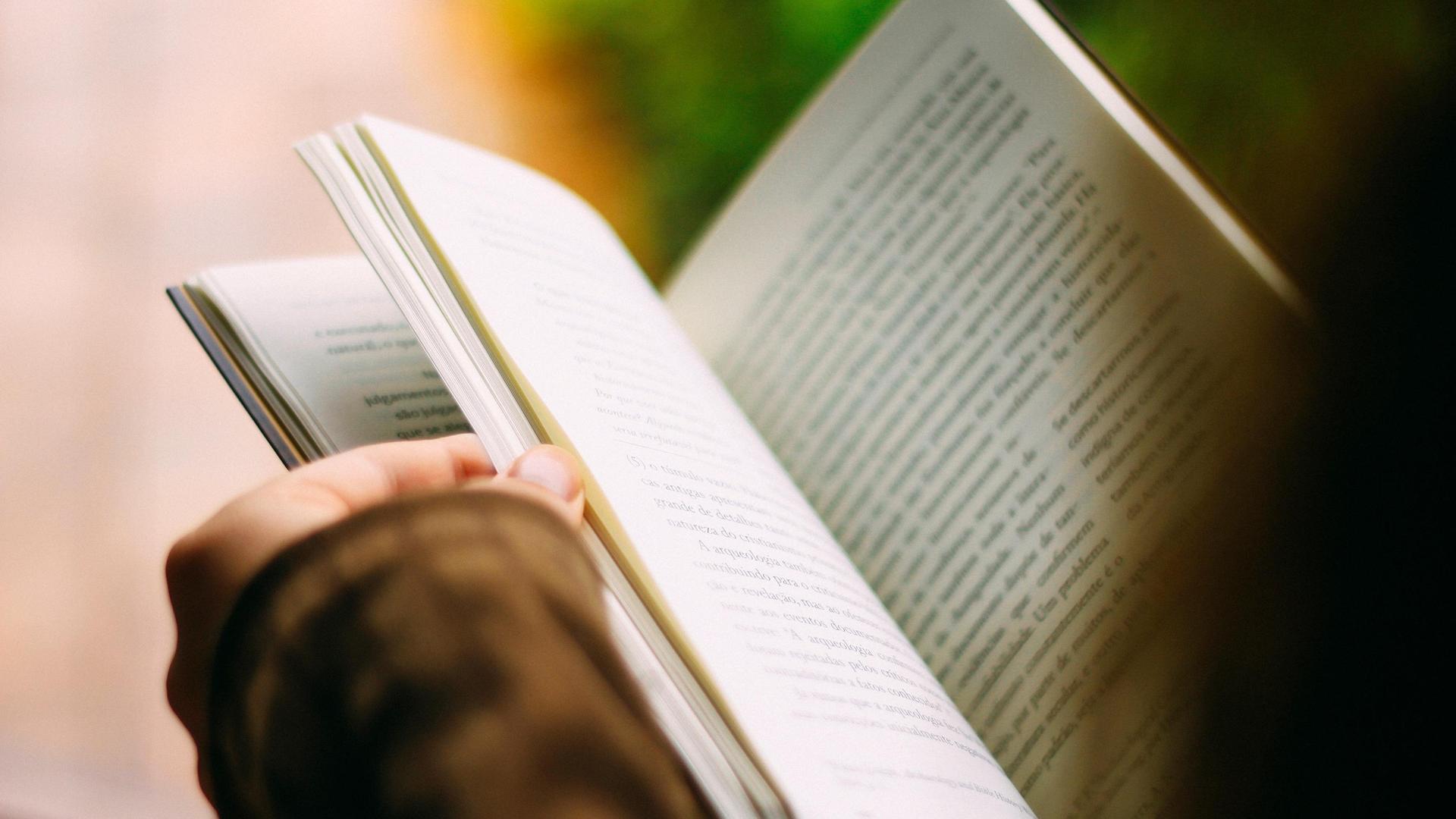 A person reading a book outdoors with focus on the pages.