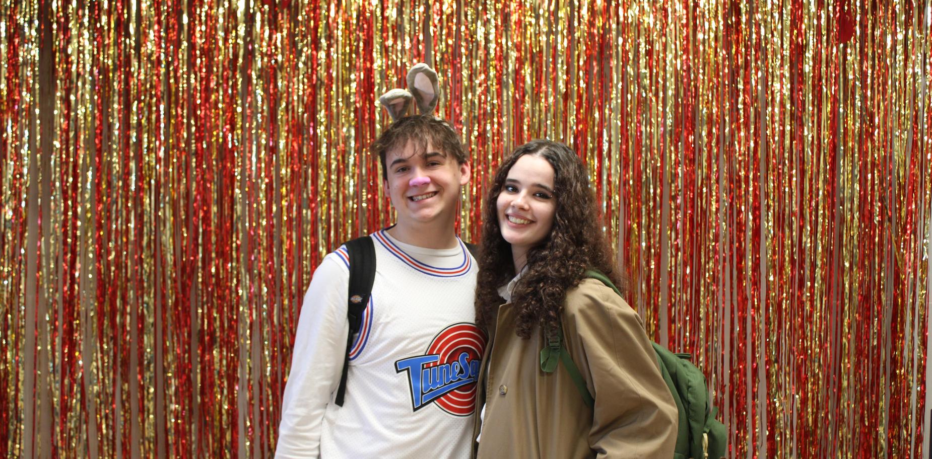 Two students in costumes pose in front of a red and silver drape.
