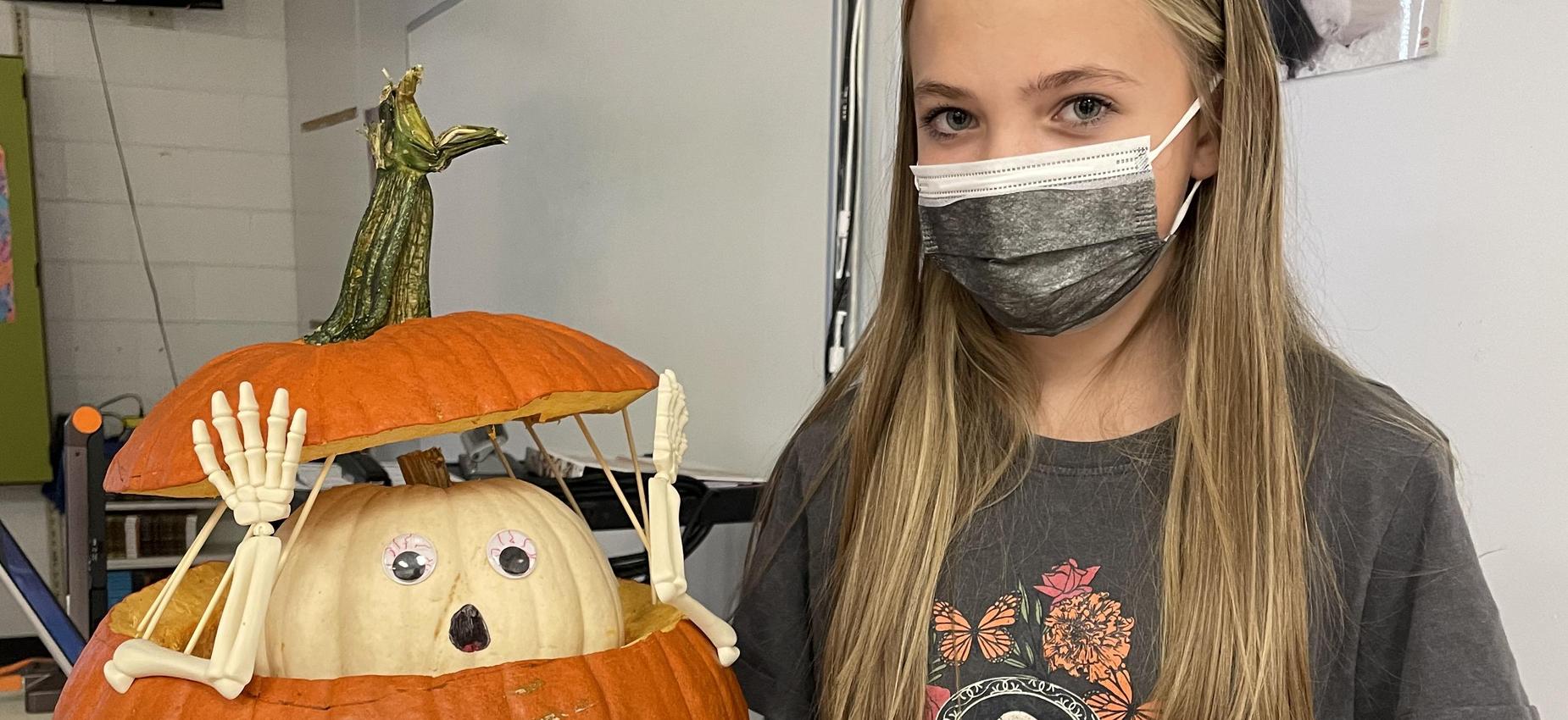 A student stands with her carved pumpkin.