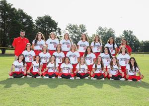 A group photo of a girls' softball team in uniforms on a grassy field.