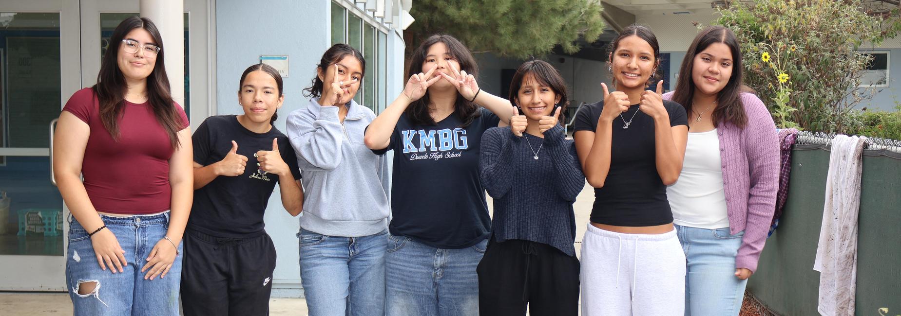 Group of seven young women smiling and posing together outdoors.