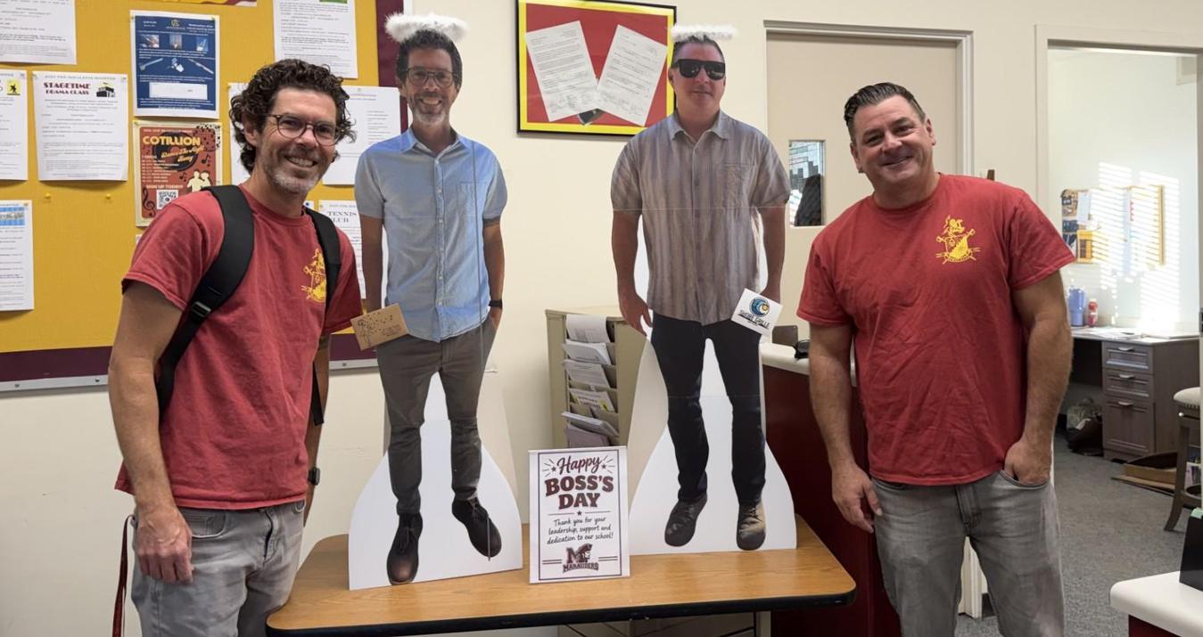 Two teachers posing with cardboard cutouts in a classroom setting.