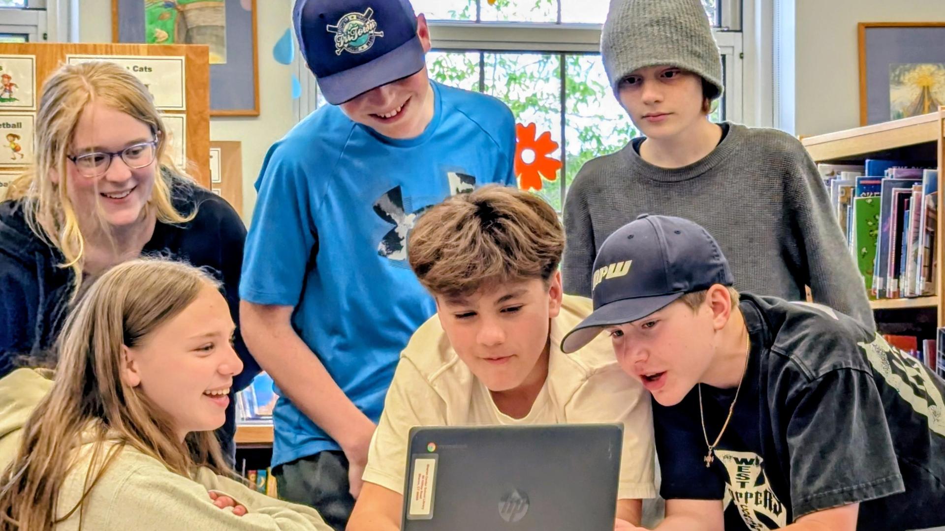 Group of children gathered around a Chromebook, engaged and smiling.