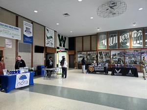 Various informational tables set up in a school lobby with attendees interacting.