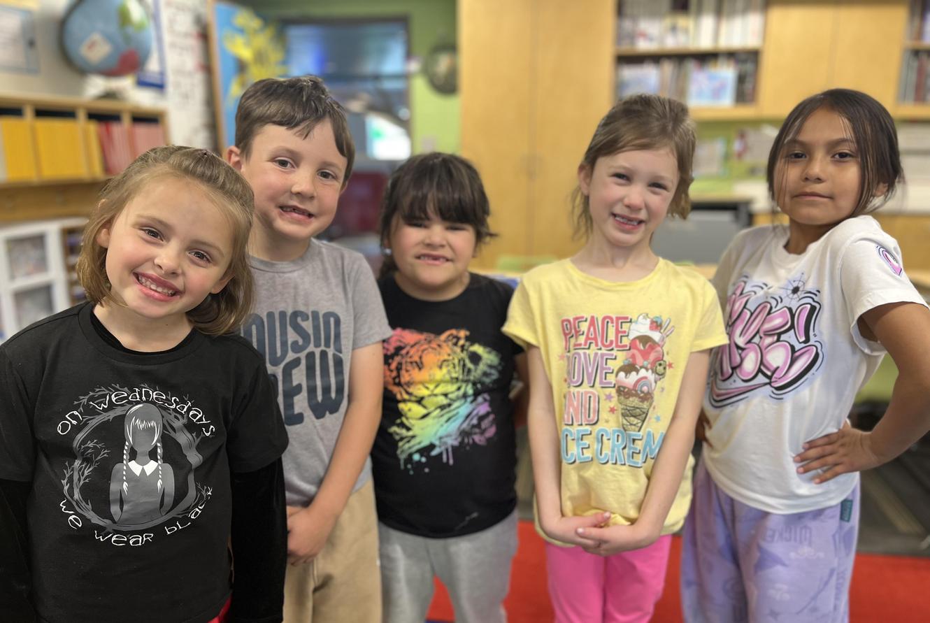 Five children smiling together in a colorful classroom setting.