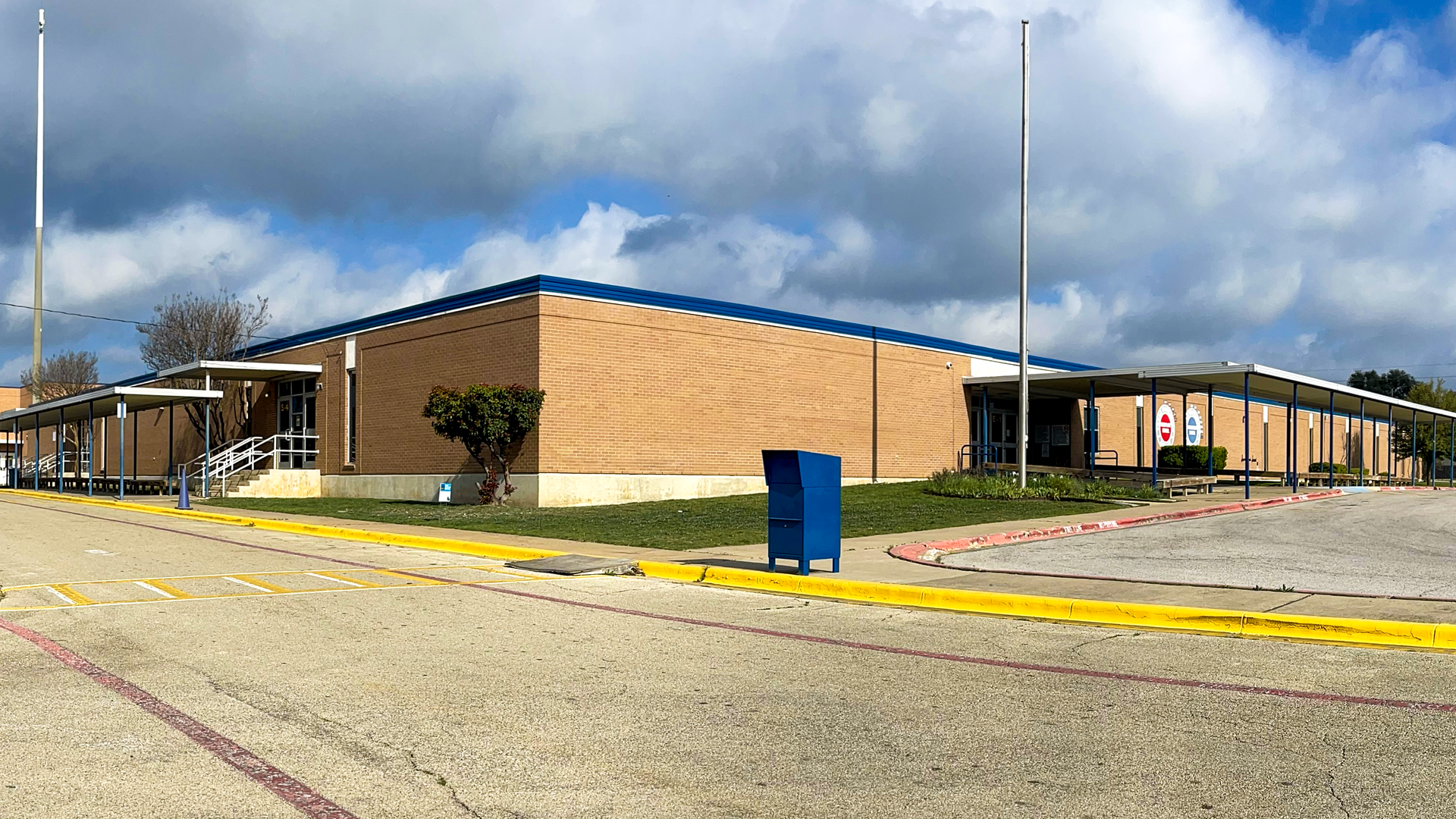 A brick school building with a blue roof and a parking area in front.