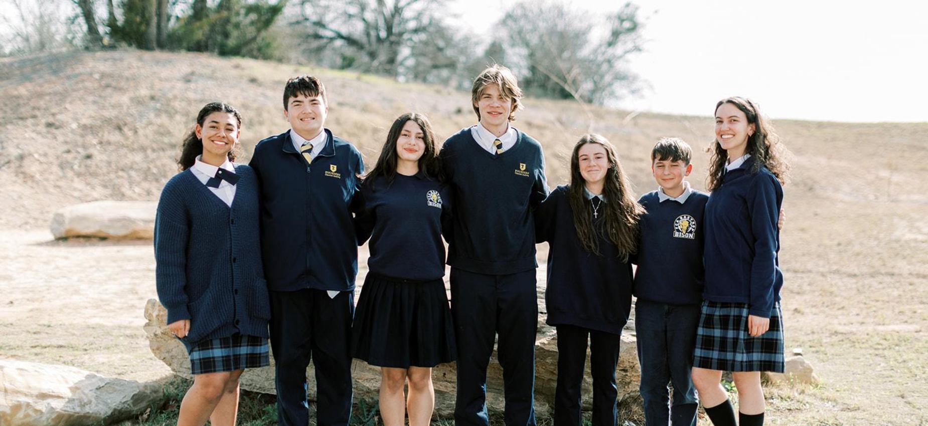 Seven upper school students in Founders uniforms stand together outside