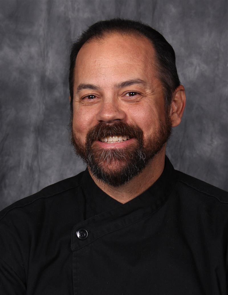 Jason Prince wearing a black chef's coat against a gray backdrop.