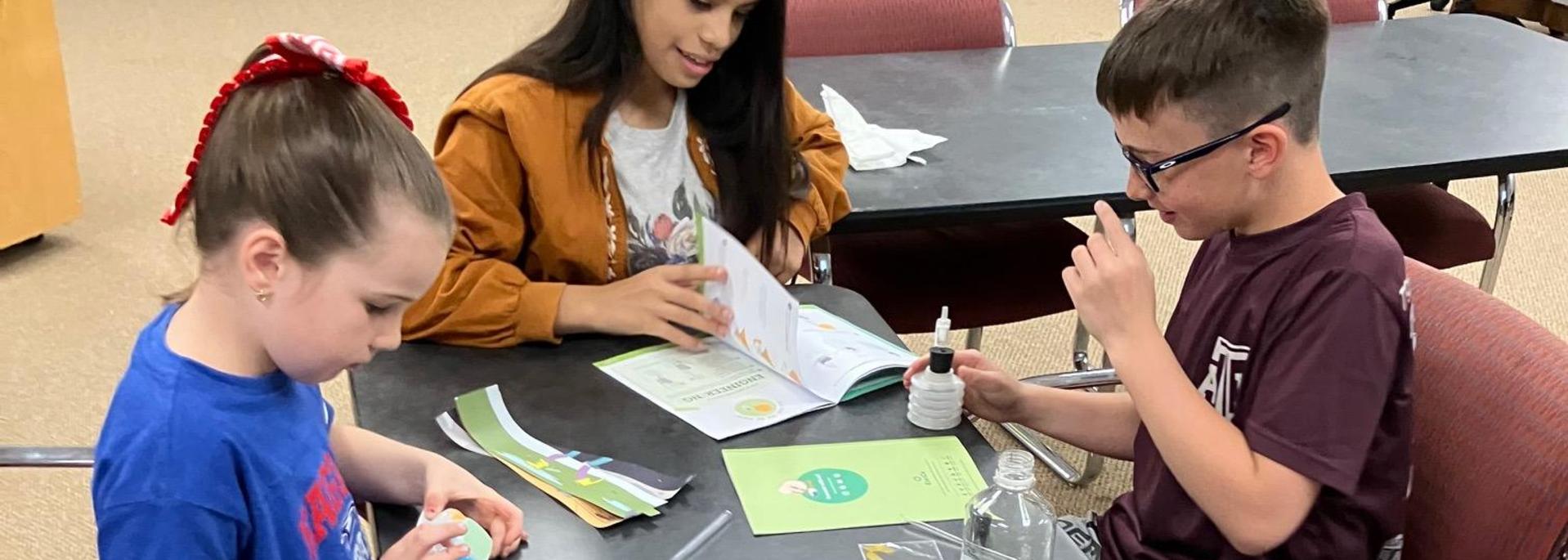 Three children engage in a crafting activity at a table filled with supplies.
