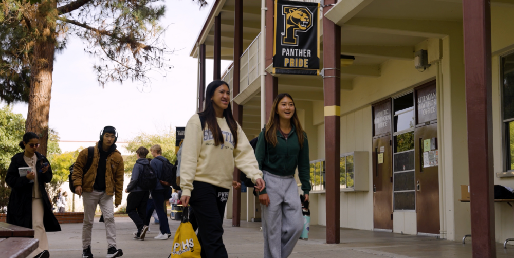 Two students walking in front of a school building under a Panther Pride banner.