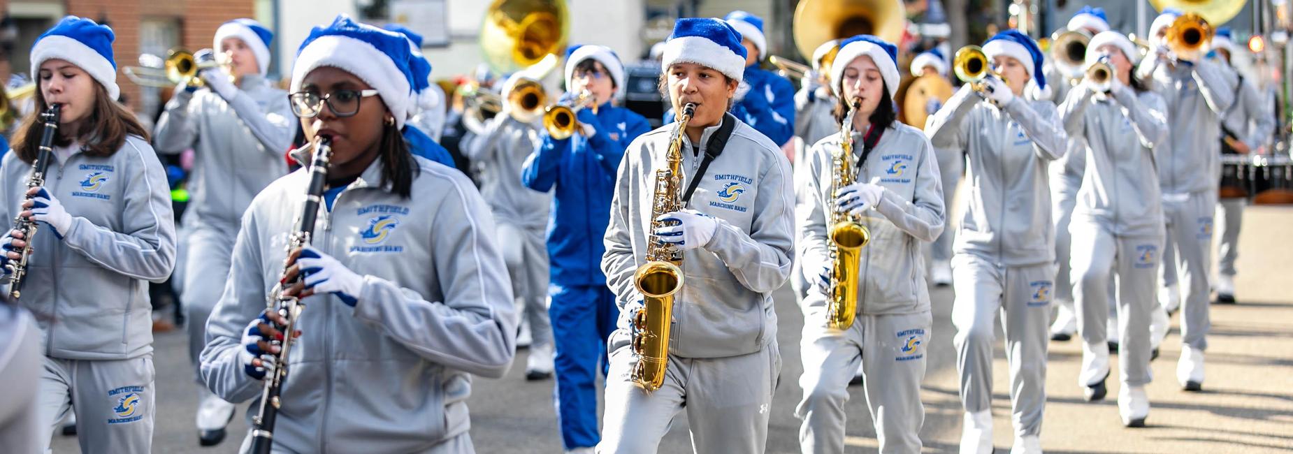 Marching band members in winter attire perform with instruments in a parade.
