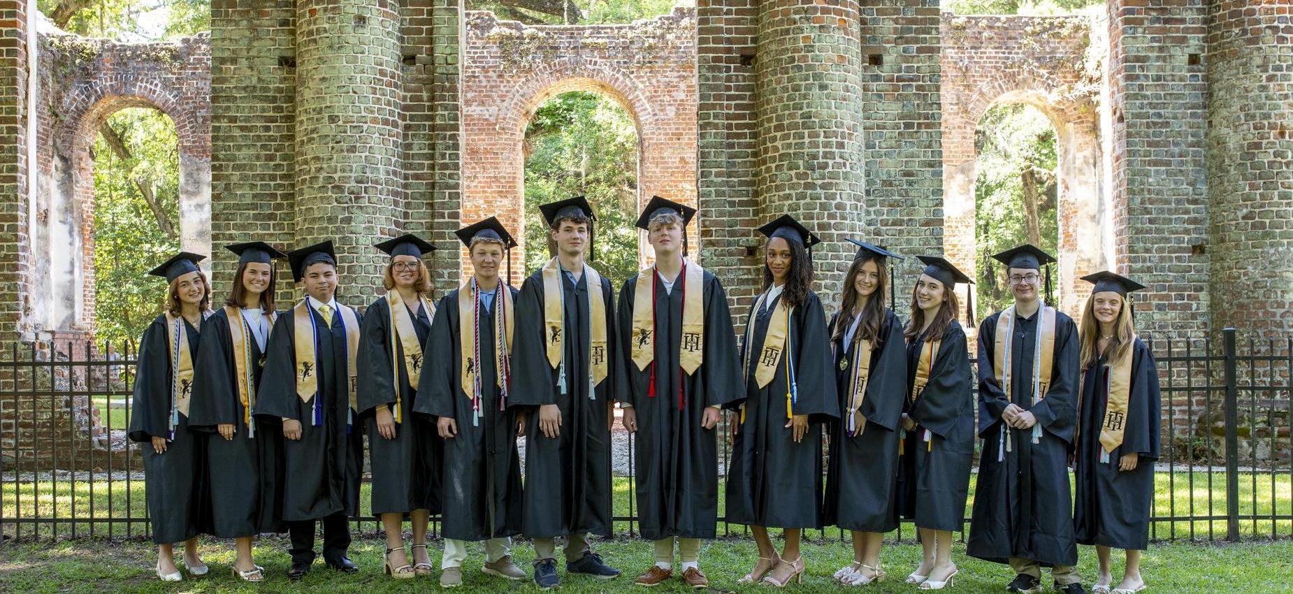 A group of graduates in caps and gowns posing together outdoors near stone ruins.