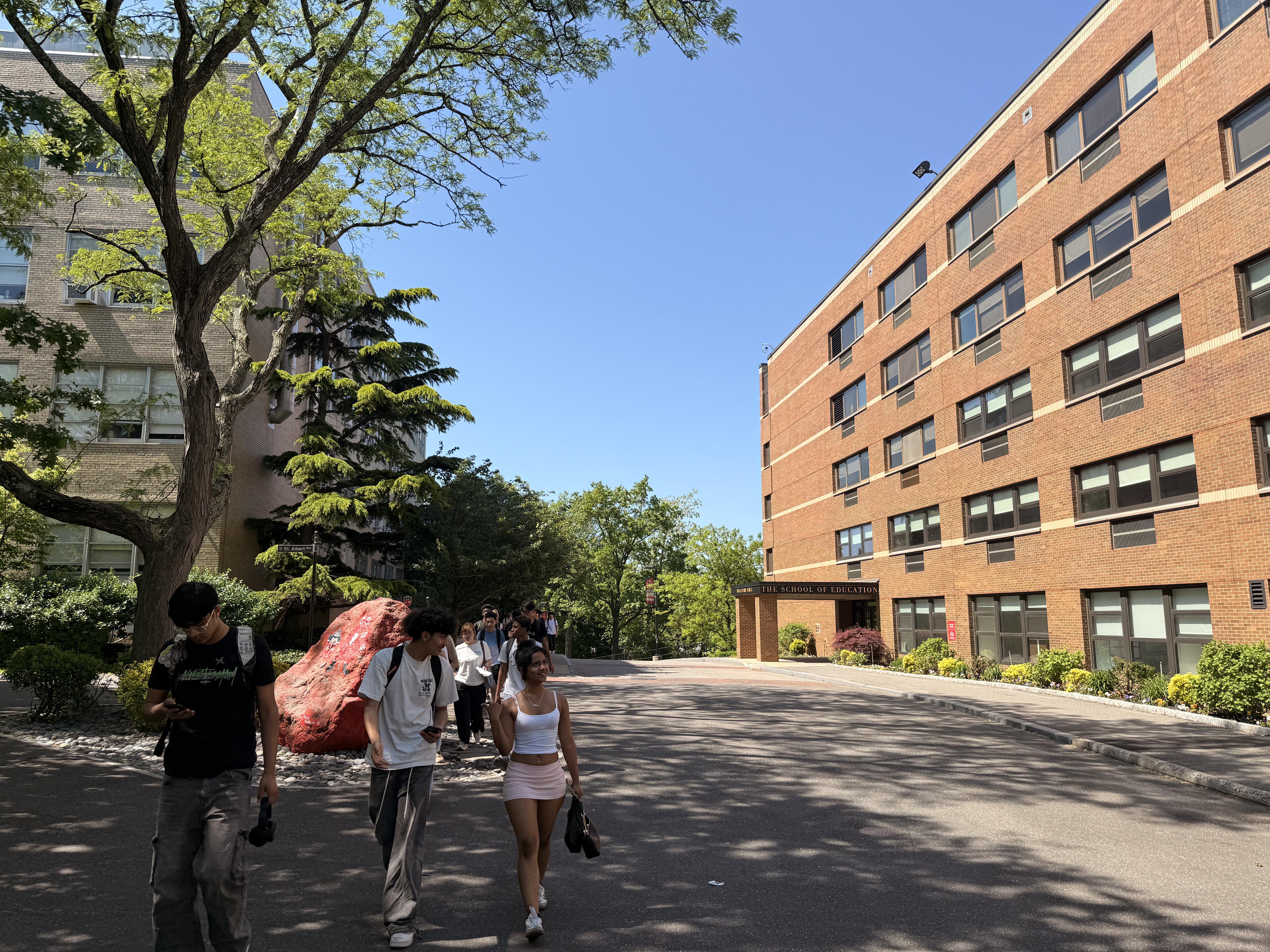 Students walking down a tree-lined path next to a brick building.