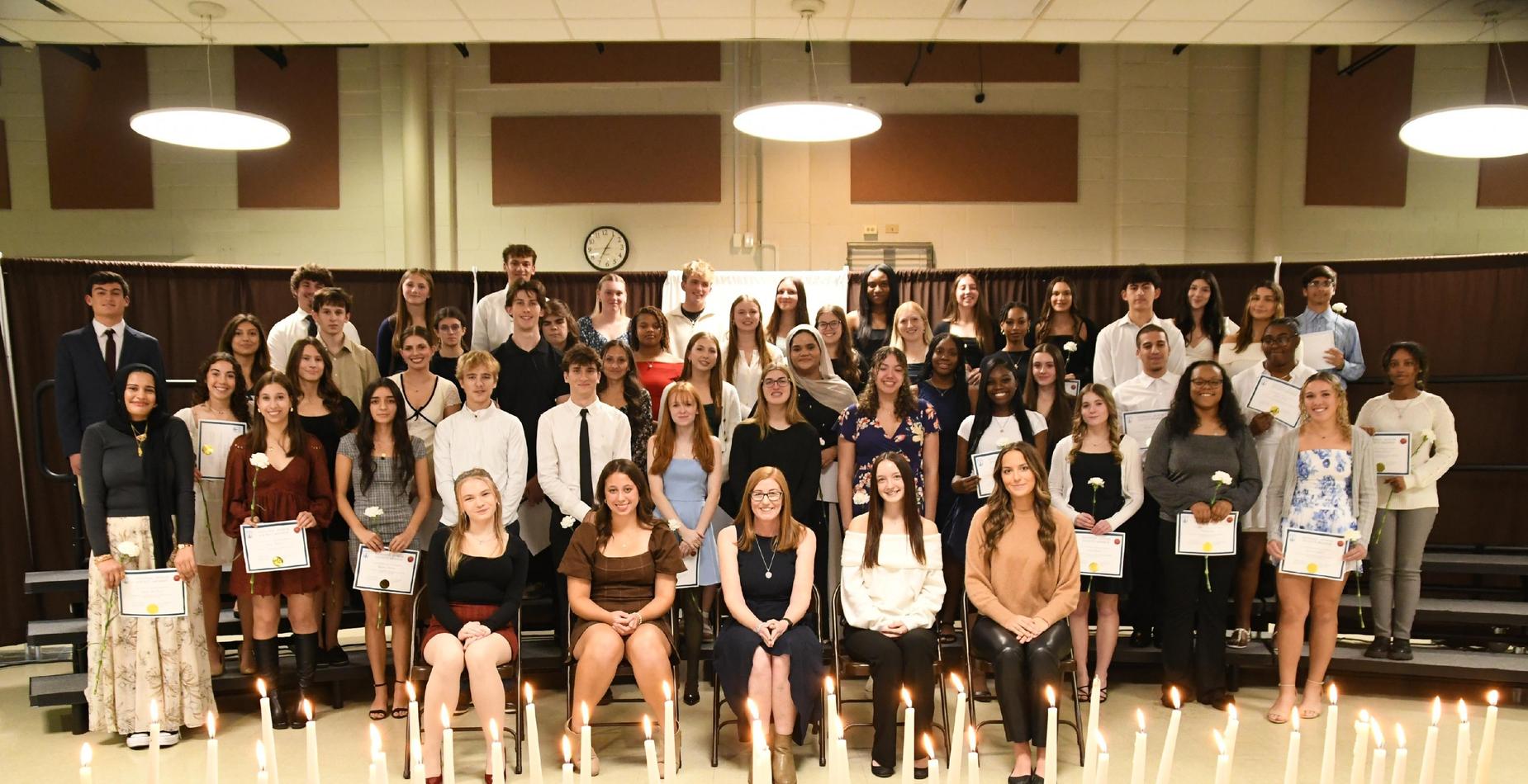 Lit candles sitting on table in front of group smiling. Front row is sitting but others are standing.
