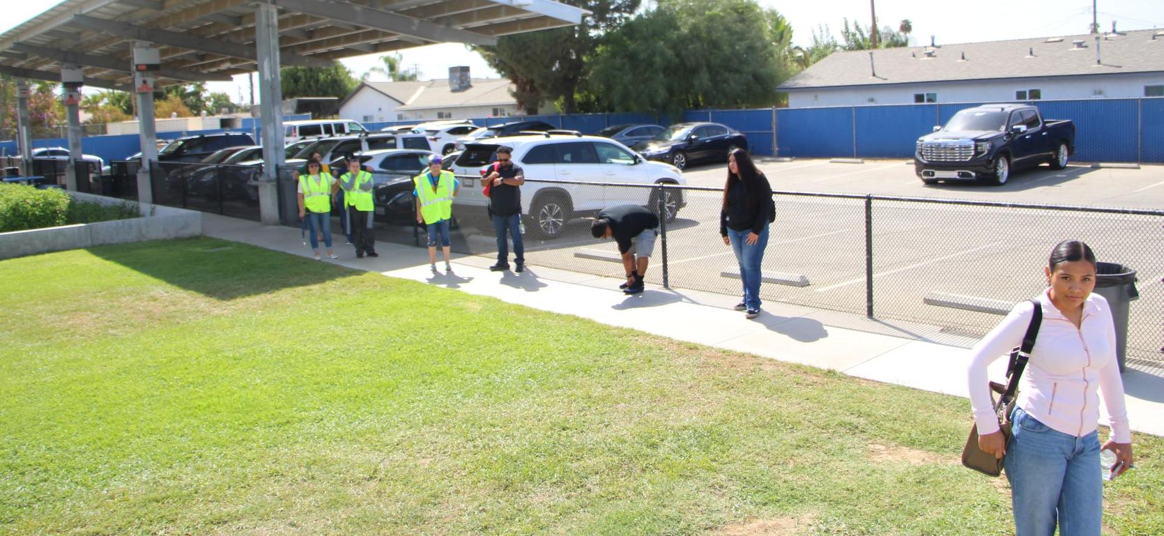 Group of people in bright vests near a parking lot by a grassy area.