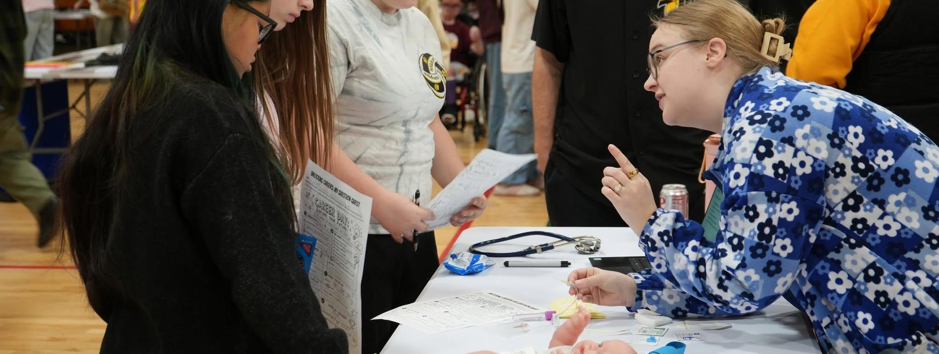 A group discussing at a table with papers and a medical model in a hall.