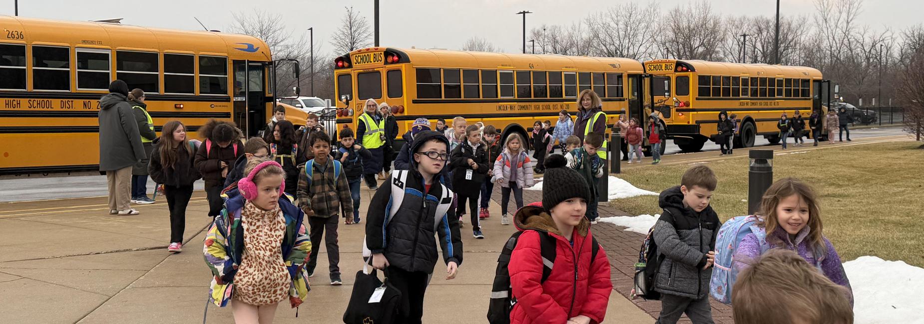 Groups of children exiting school buses in a school parking lot.
