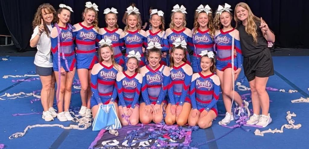 group of middle school cheerleaders in uniforms posing in front of their Champion winning flag and gold medals