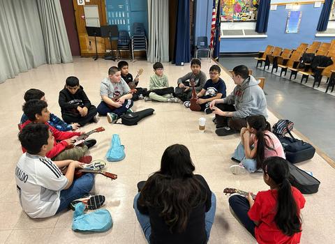 Students sitting on stage playing ukelele.