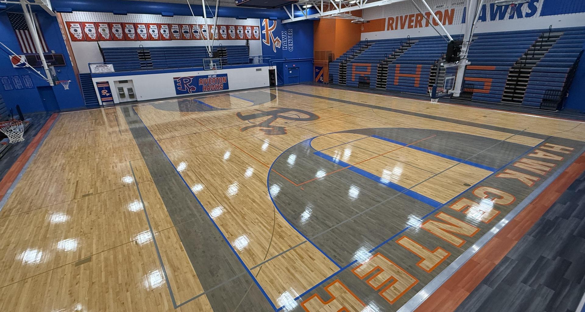 Basketball court with logo, bleachers, and colorful team banners.