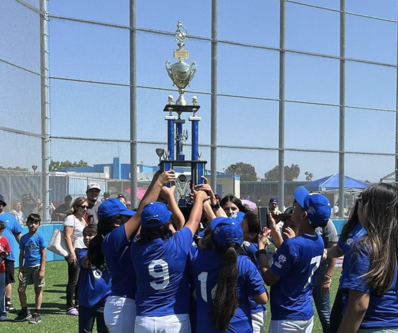 about 10 students in baseball uniforms lift trophy