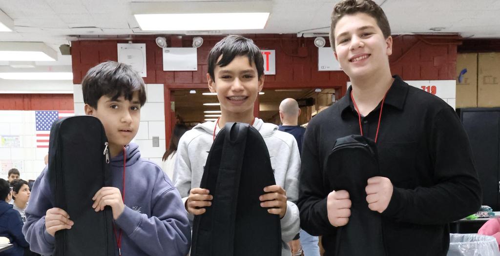 Three boys standing.  One boy is holding a guitar case.