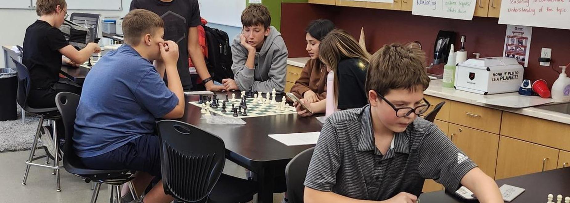 Students playing chess in a classroom setting, focused on their game at tables.