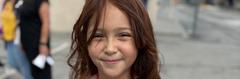 Smiling girl with brown hair and freckles, posing outdoors.