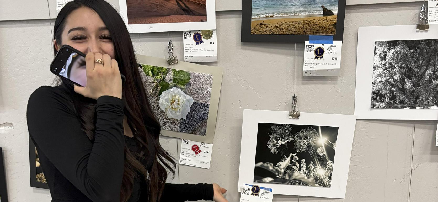 A woman sitting with long hair by a wall of various framed art pieces.