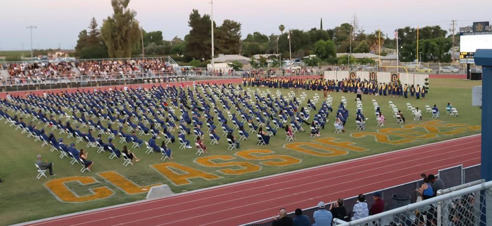 Wide shot of a large graduation ceremony with attendees and graduates in caps and gowns.