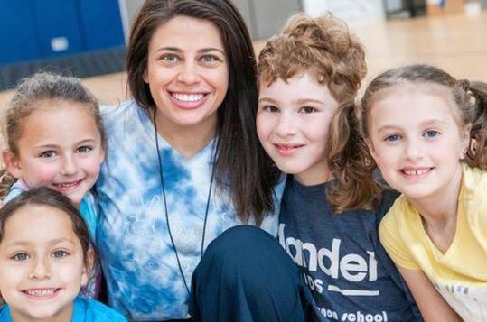 A smiling group of five kids and an adult in a gym setting.