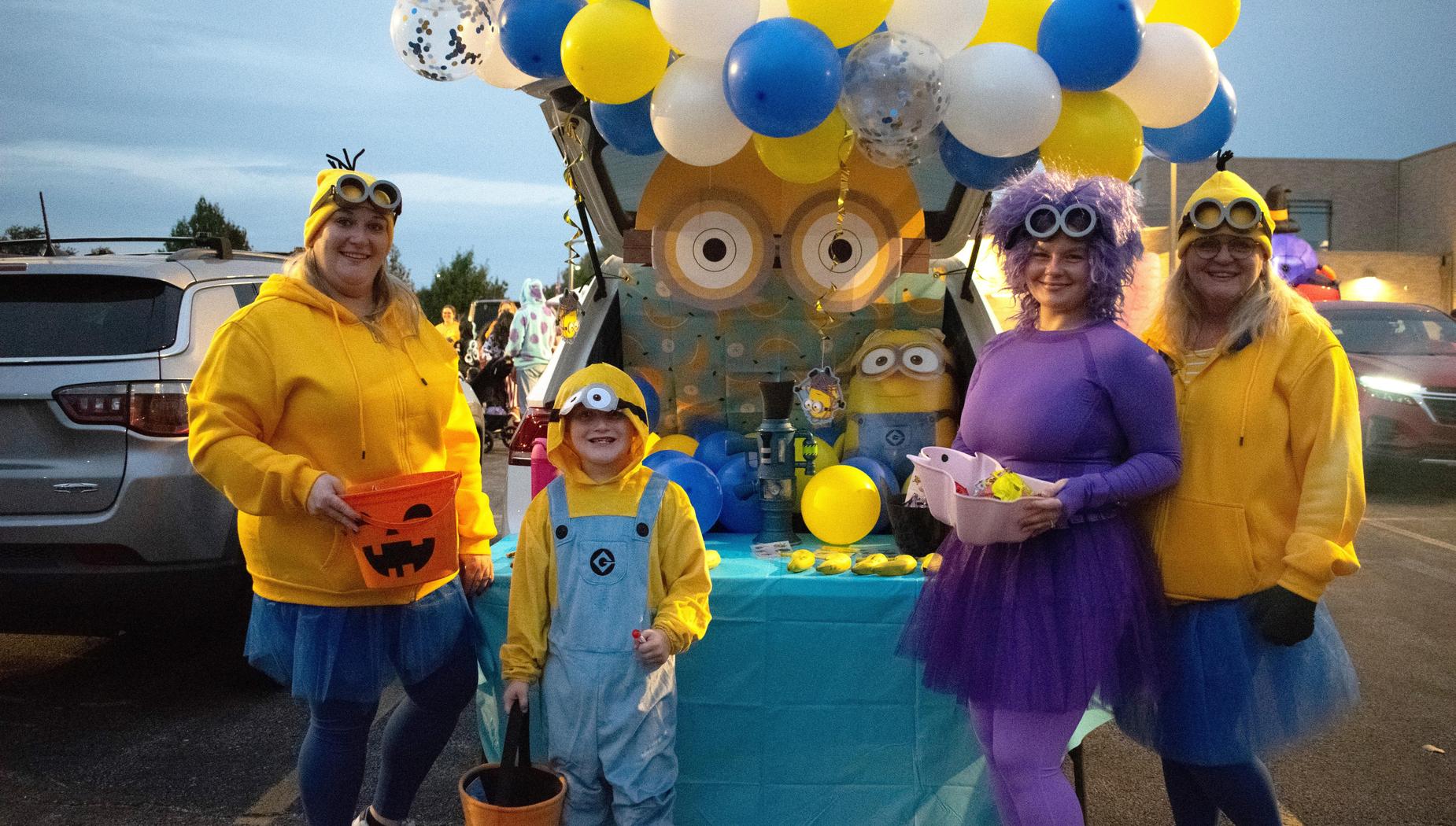 Group of women and a child in Minion costumes by a colorful trunk display.