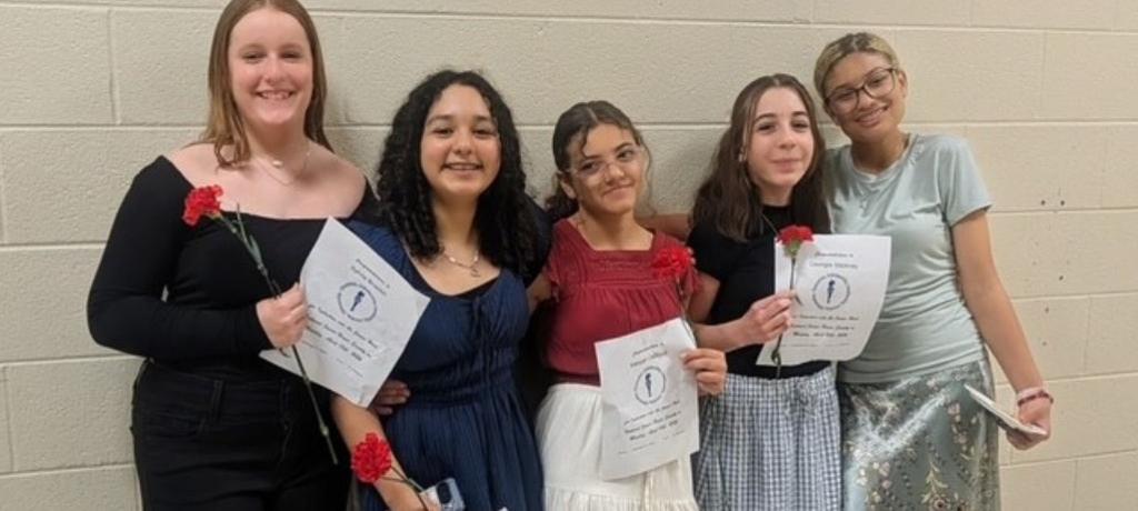 five girls pose with red carnations and ceremony programs