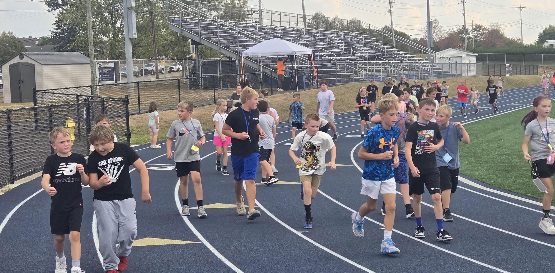 Group of children walking on a running track with bleachers in the background.