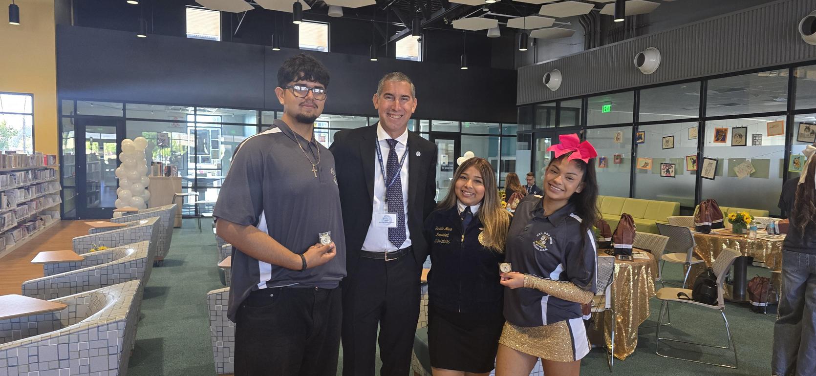 Four people posing in a library, smiling and holding awards.