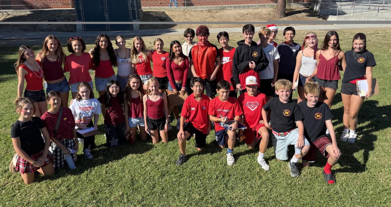Group of students posing together in red and white attire in a grassy area.